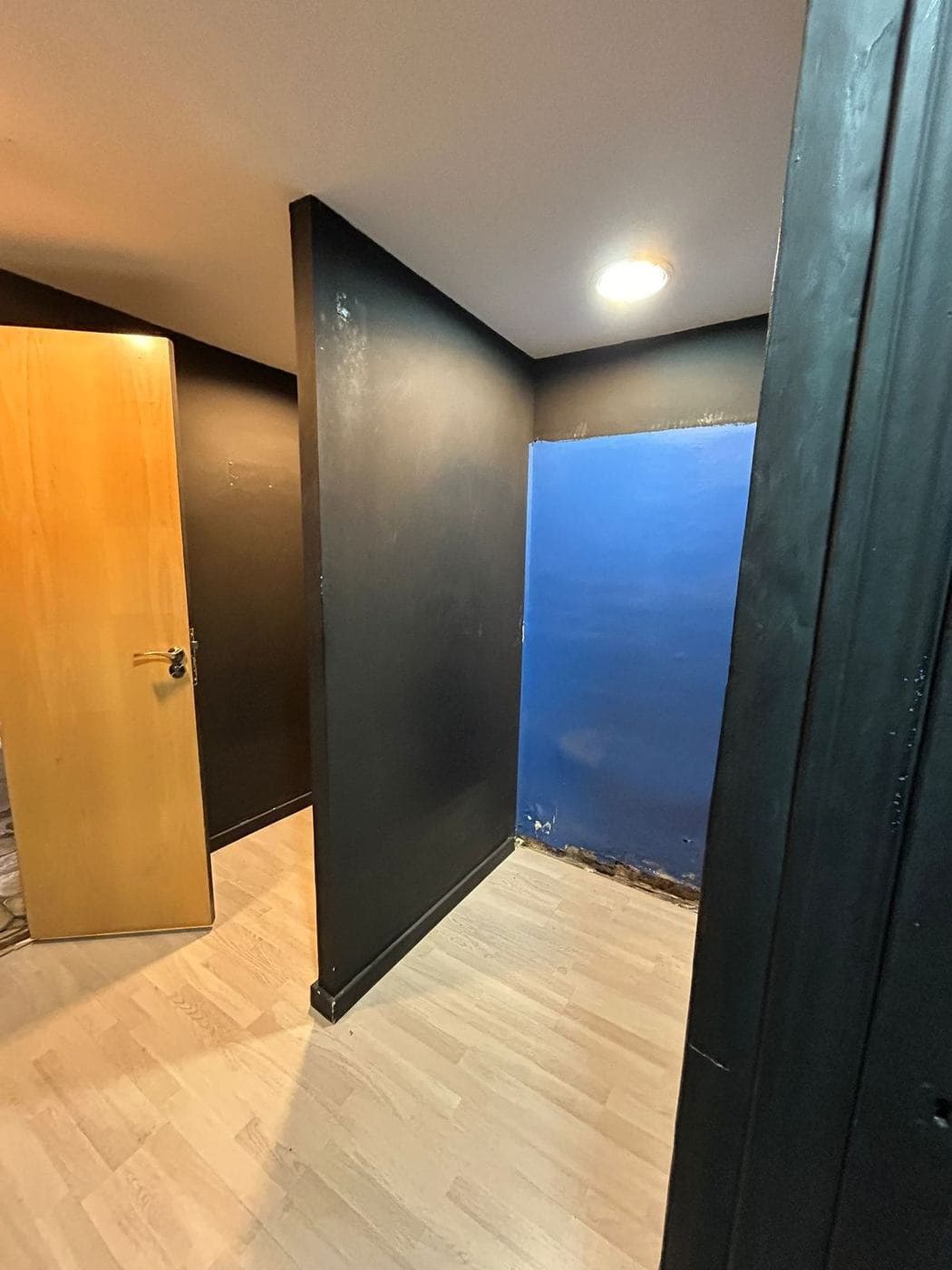 Tabiques negro y azul y puerta de madera clara en el local antes de la obra