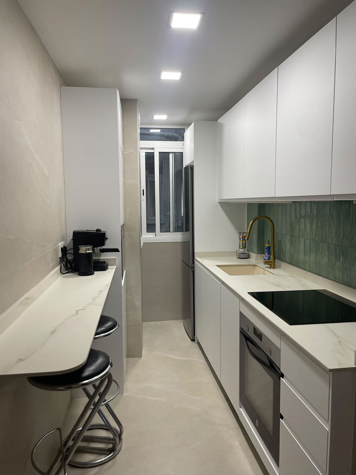 La misma cocina reformada: muebles blancos, azulejo verde y barra