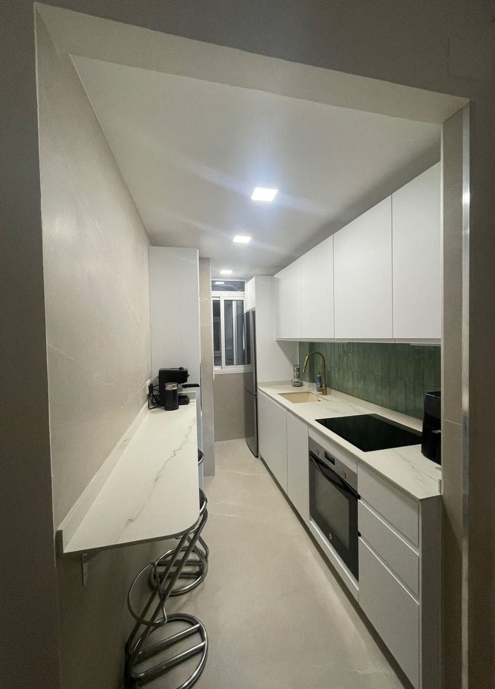 Cocina estrecha reformada con barra de desayuno y una línea de muebles blancos