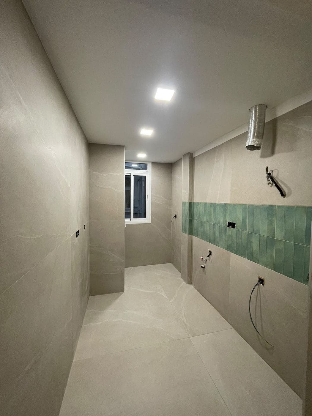 Cocina durante la obra: gres de gran formato en paredes y suelo, frente verde colocado y muebles pendientes