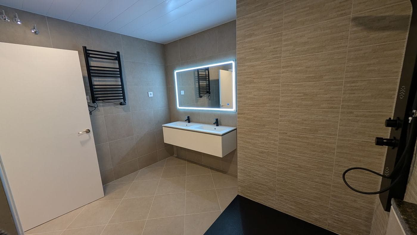 Baño con espejo rectangular retroiluminado, mueble de lavabo y toallero negro