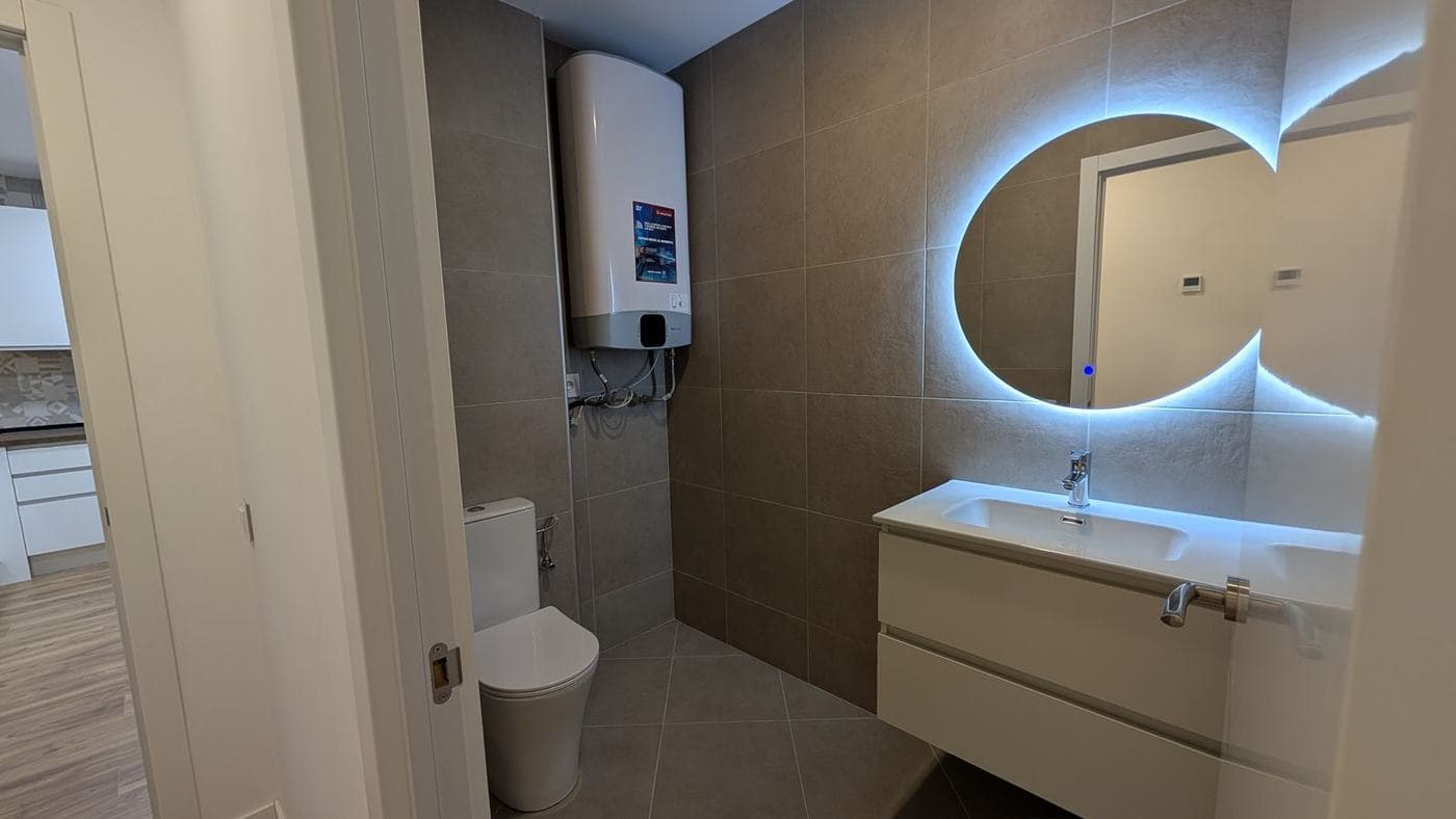 Baño con espejo redondo retroiluminado y mueble de lavabo blanco