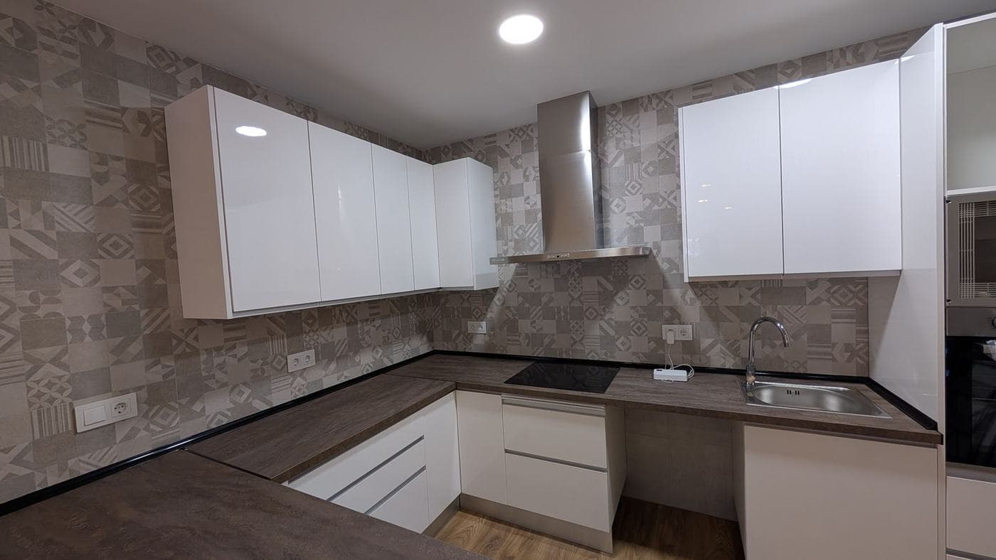 Cocina blanca en forma de L con encimera oscura y frente de azulejo hexagonal