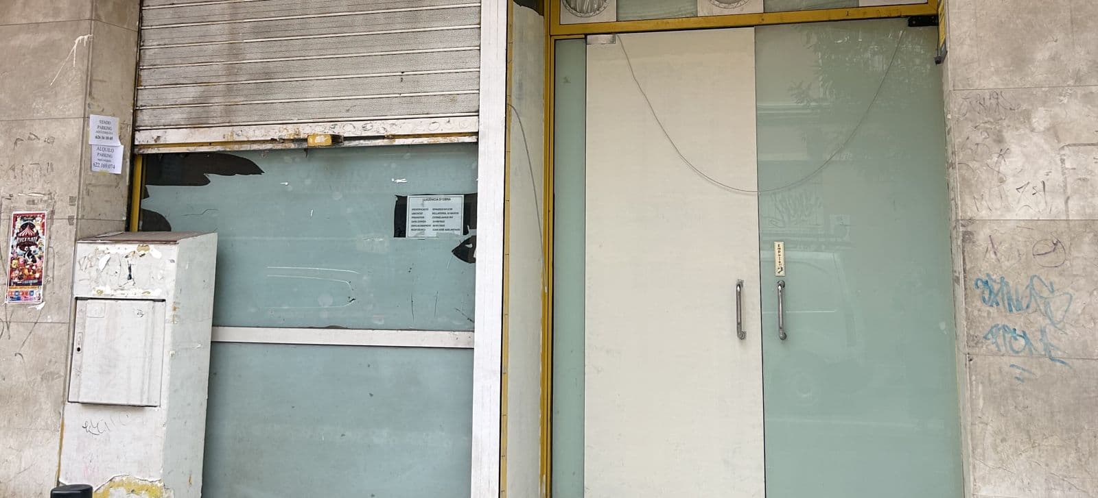 Fachada del local antes: persiana metálica y puerta de cristal con marco amarillo
