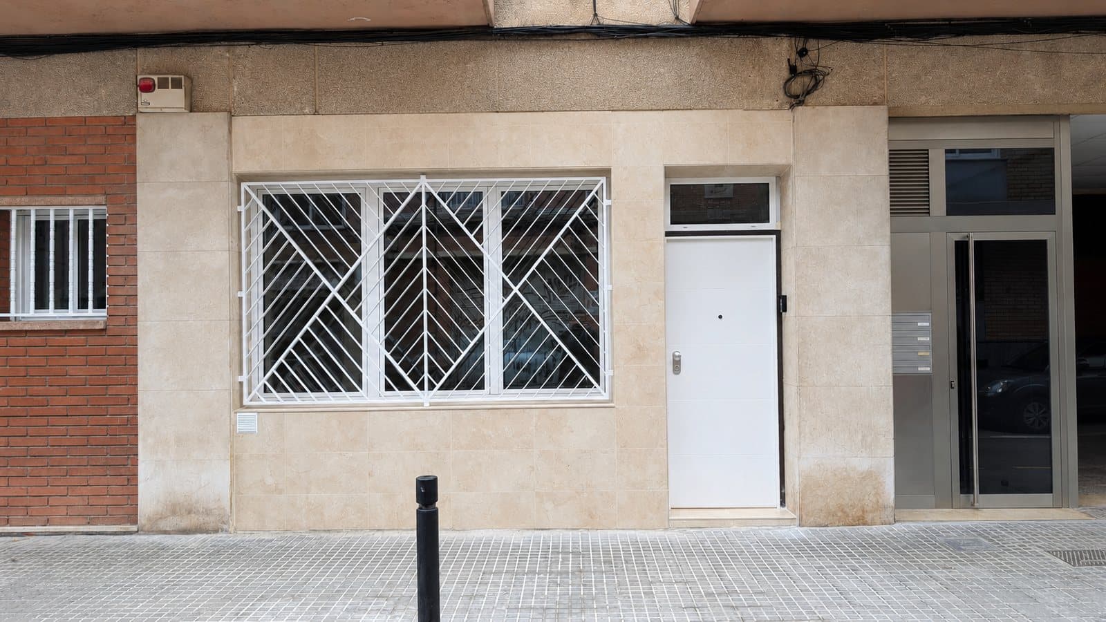 Fachada de la vivienda después: ventana con reja blanca y puerta de entrada nueva