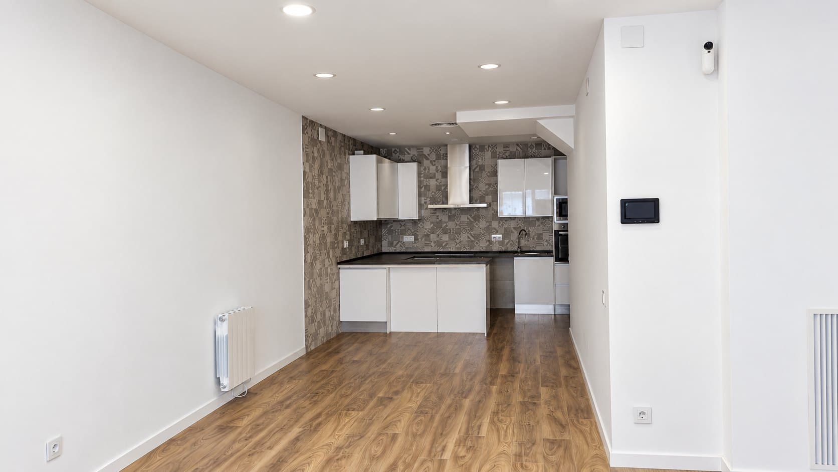 Salón de una vivienda reformada y vendida: cocina abierta al fondo y suelo de madera
