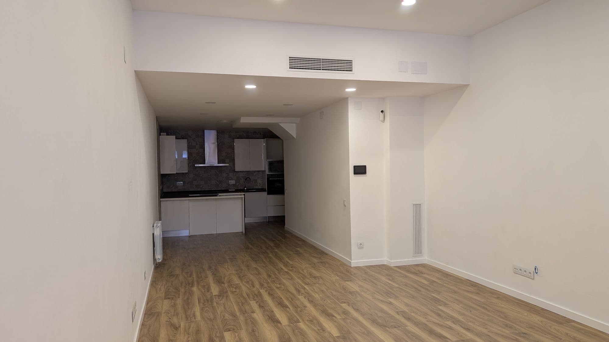 Salón de la vivienda con la cocina abierta al fondo y suelo de madera