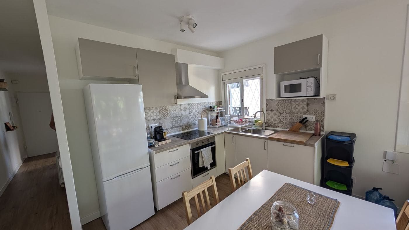 Cocina abierta con muebles claros, frente de azulejo y ventana