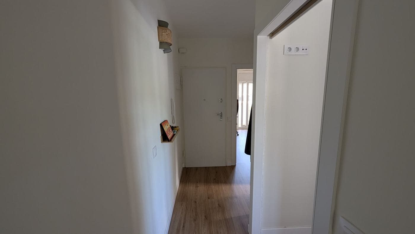 Recibidor con suelo de madera clara y puerta de entrada al fondo