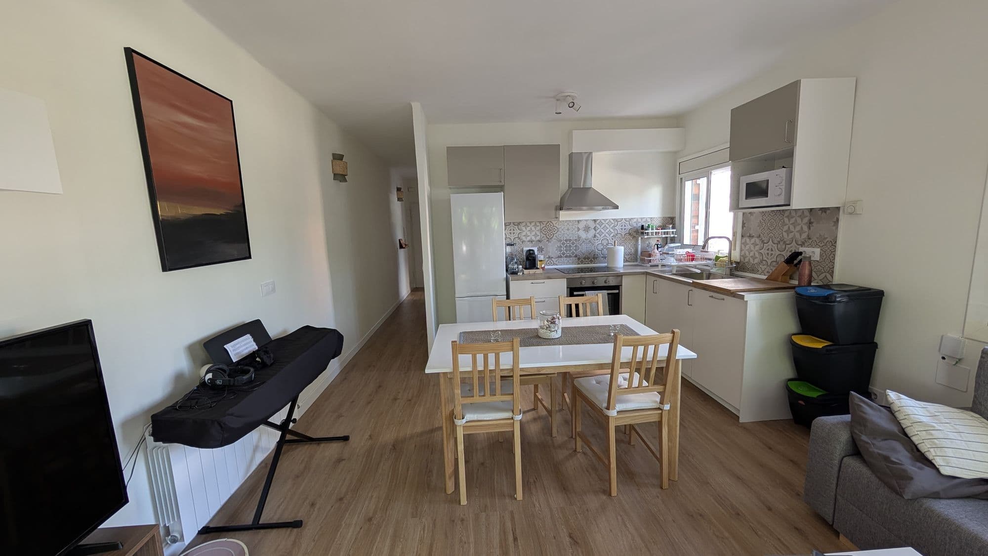Salón con la cocina abierta al fondo, mesa de comedor y suelo de madera