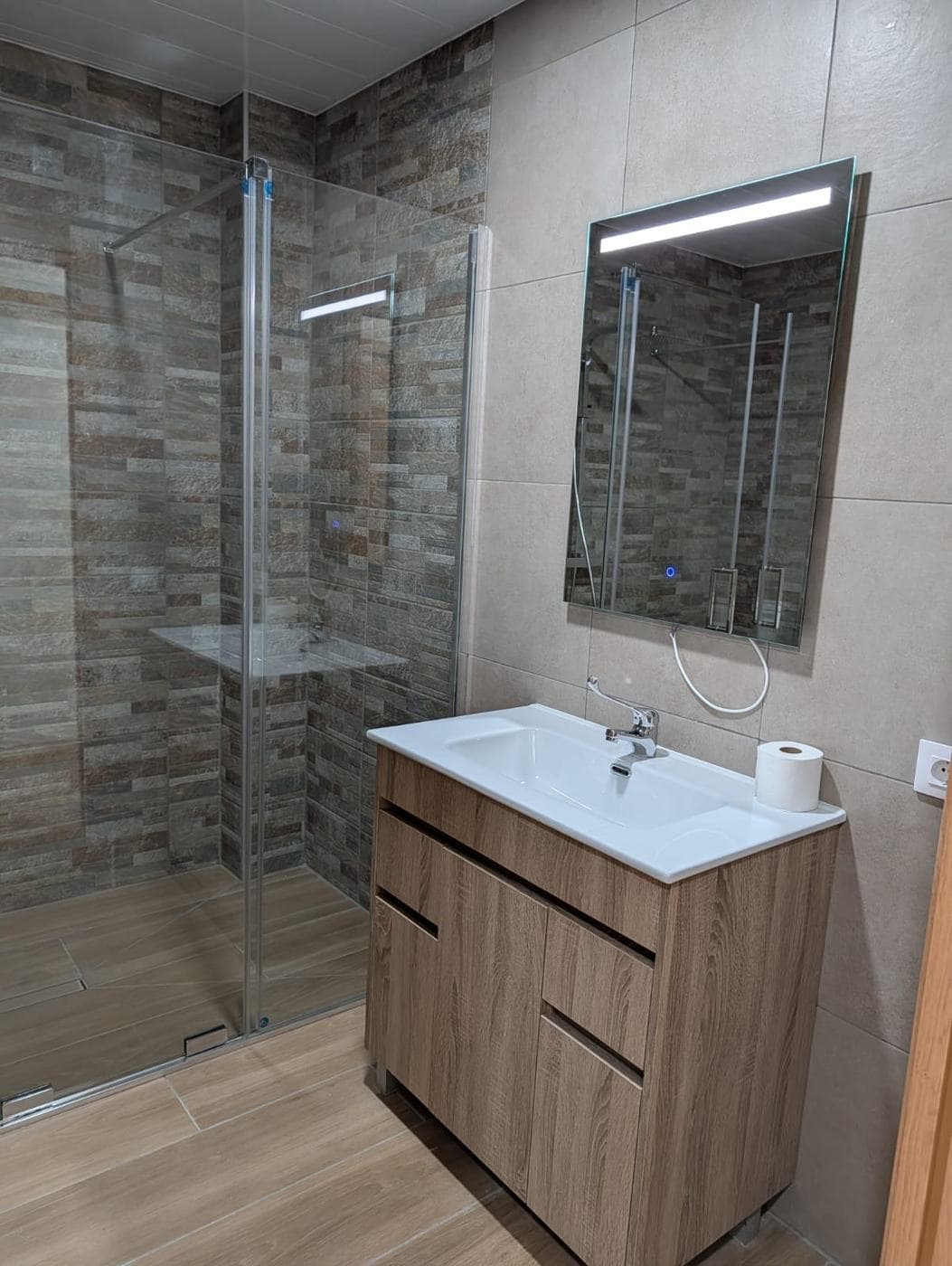 Segundo baño con mueble de lavabo de madera y ducha con mampara