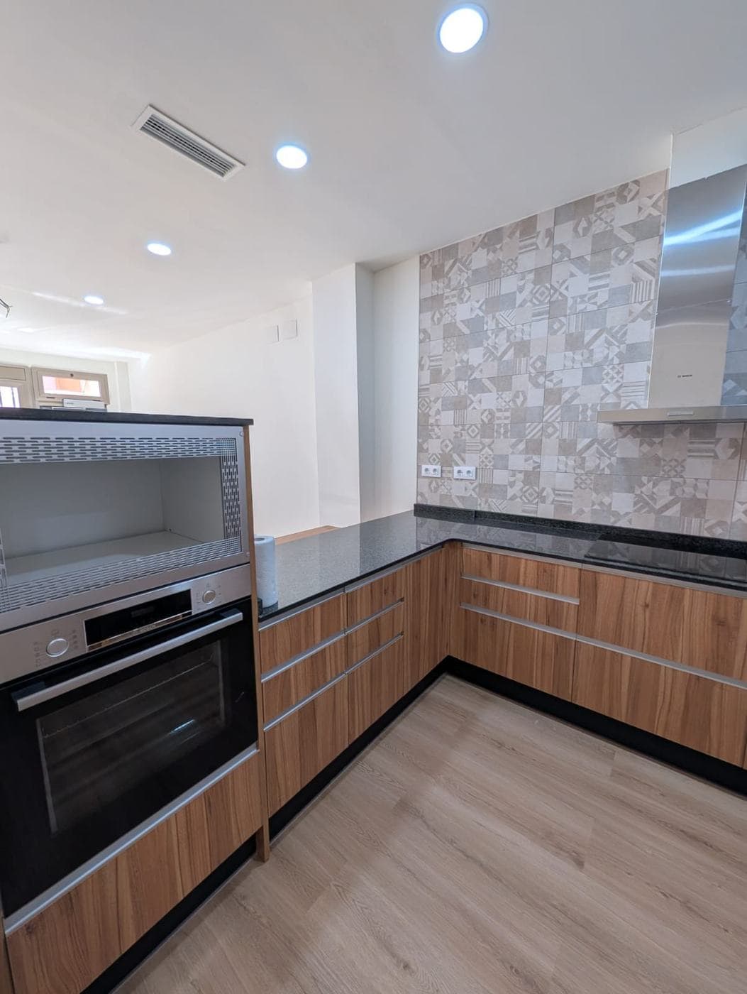 Cocina con muebles de madera, encimera oscura y frente de azulejo estampado