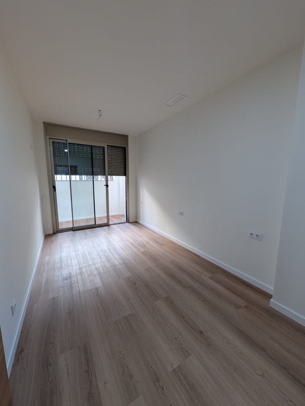 Dormitorio con ventanal al fondo y suelo de madera