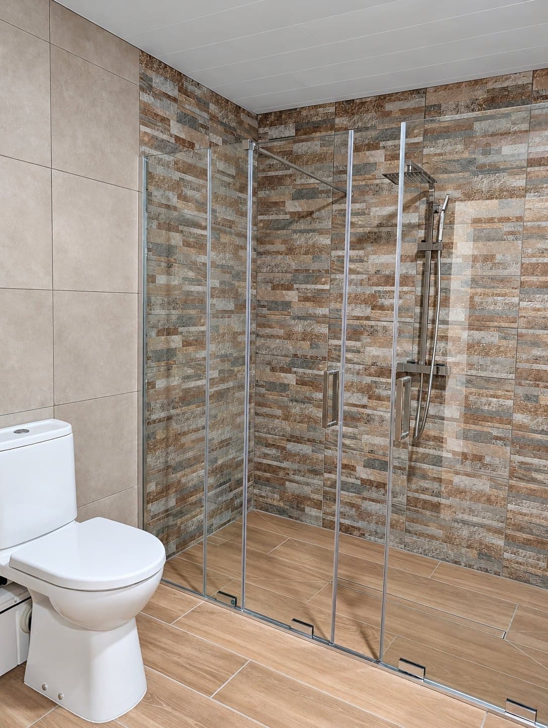 Baño con ducha a ras de suelo, mampara corredera y revestimiento tipo piedra