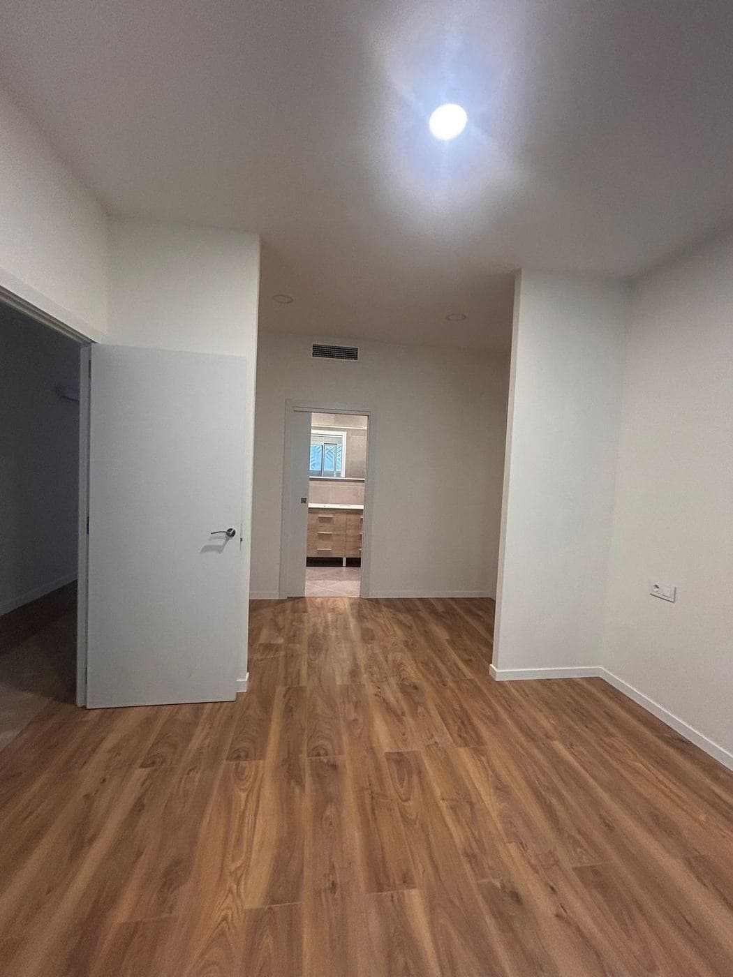 Distribuidor de una de las viviendas: paredes blancas, suelo de madera y puertas hacia el baño y las habitaciones