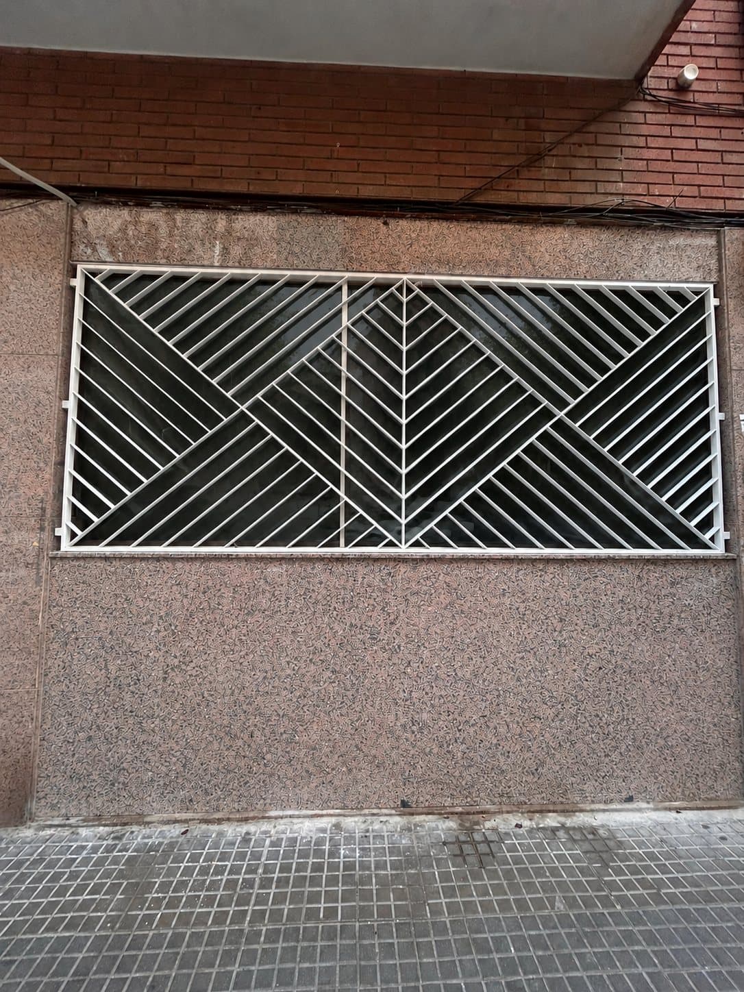 Fachada después de la reforma: ventana con celosía metálica blanca sobre el aplacado de piedra