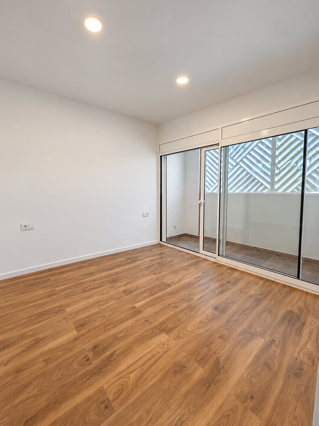 Salón de una de las viviendas: suelo de madera y ventanal corredero hacia la terraza, con celosía metálica blanca